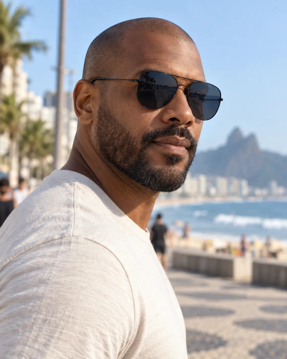 Homem usando óculos de sol masculino aviador preto Aston LURVANI, com lentes azul fumê e ponte dupla, em calçadão próximo ao mar.