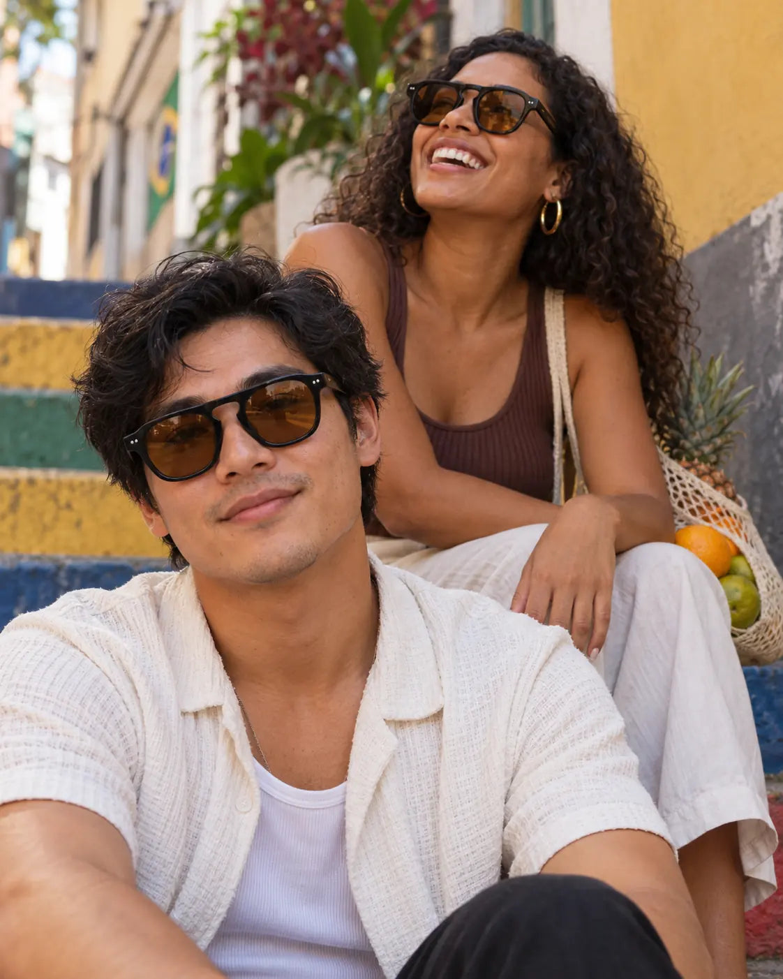 Homem e mulher usando óculos de sol unissex quadrado preto modelo Âmbar LURVANI, com lentes âmbar, em retrato de moda.