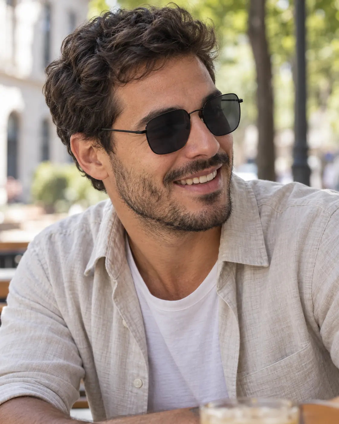 Homem usando óculos de sol masculino quadrado preto Norden LURVANI, com armação metálica fina e lentes fumê, em ambiente urbano ao ar livre.